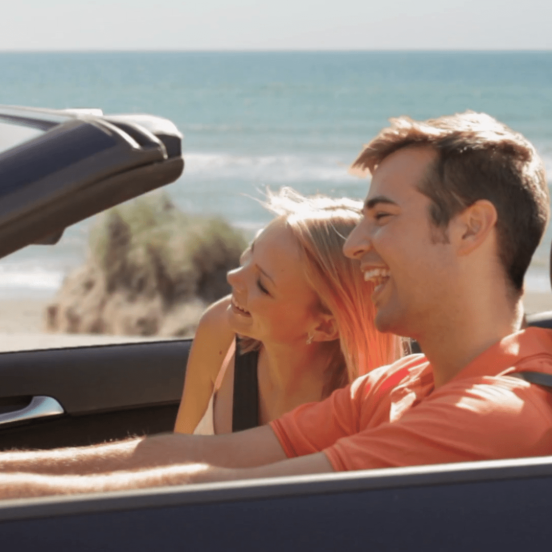 a man smiling and driving the car with a woman beside him.